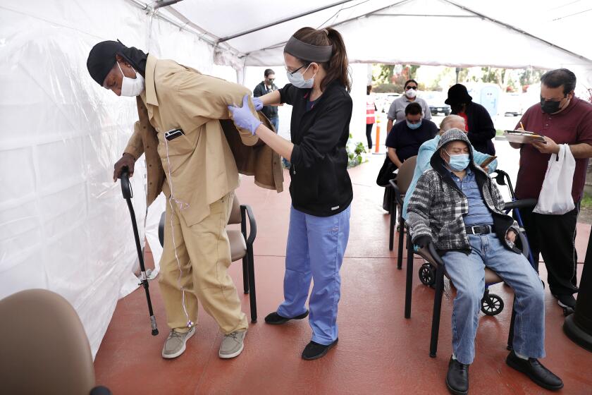 LOS ANGELES-CA-MARCH 22, 2021: James Smith, 64, of Los Angeles, left, gets help with his jacket after receiving his vaccination by nurse practitioner Laura Fisher, center, at Kedren Community Health Center in South Los Angeles on Monday, March 22, 2021. (Christina House / Los Angeles Times)