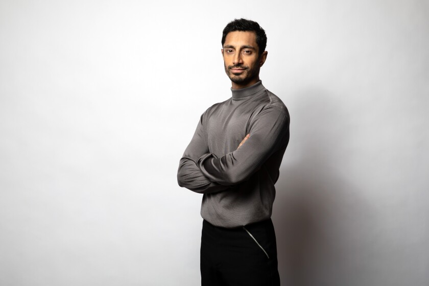 A portrait of actor Riz Ahmed wearing a satiny gray turtleneck. 