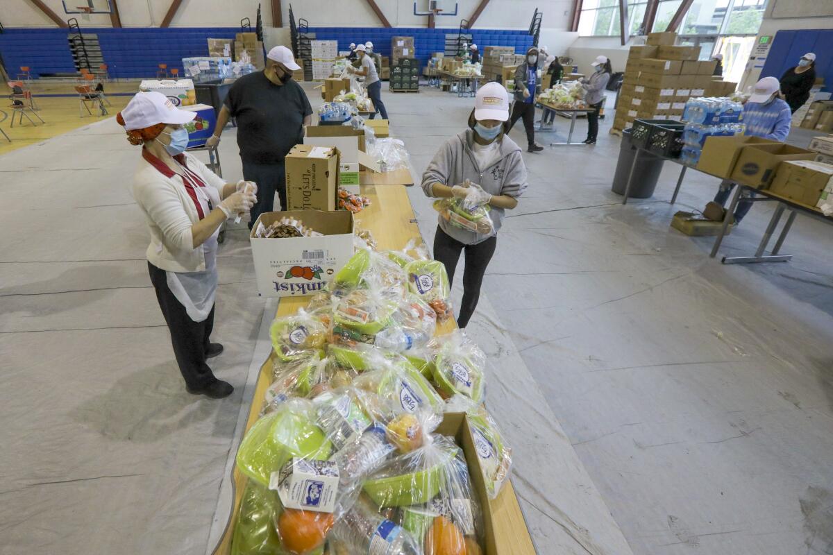 Los voluntarios trabajan en el gimnasio de la Escuela Secundaria Byrd preparando paquetes de alimentos para un centro de comida para llevar.