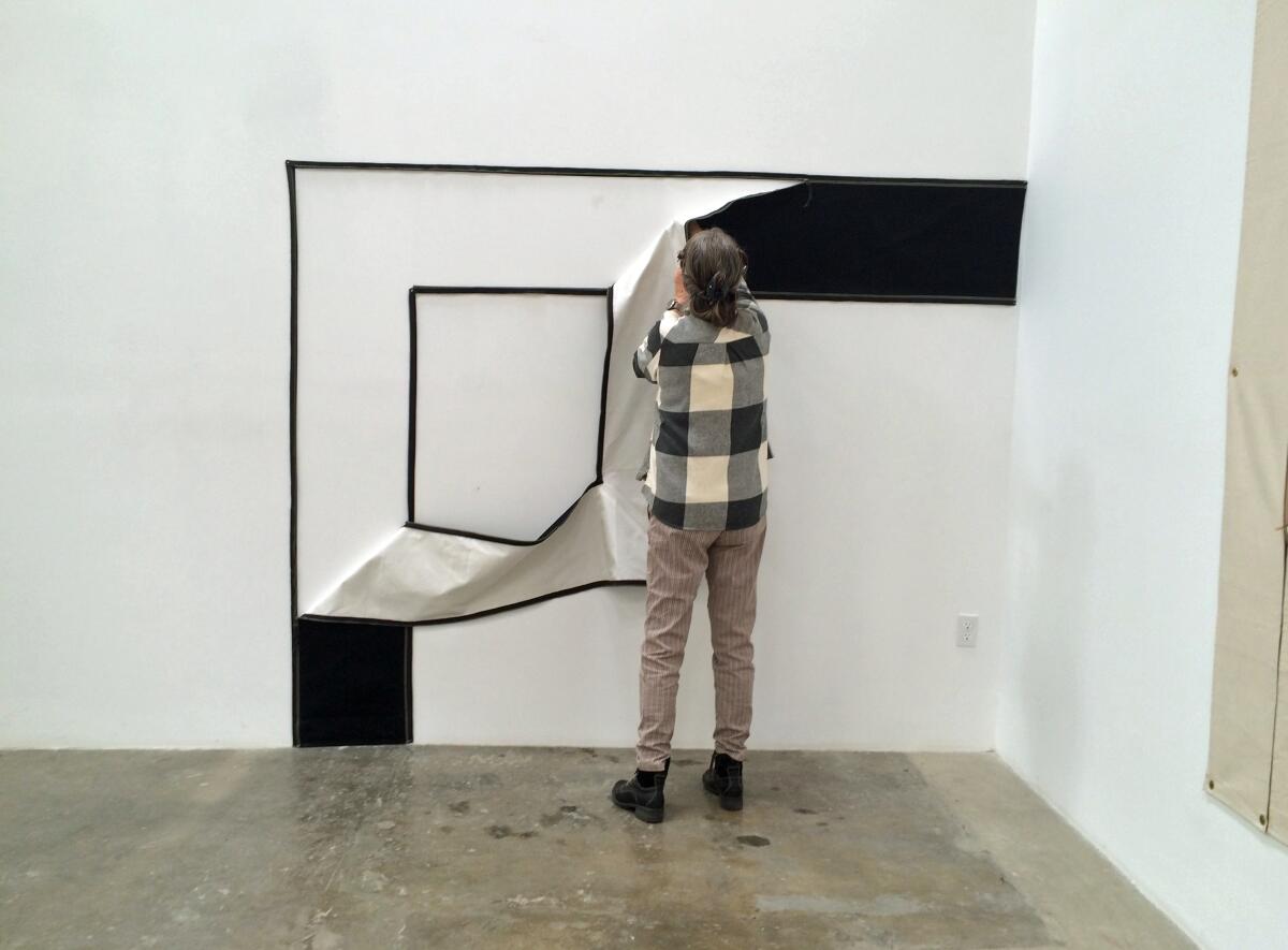 Karen Carson manipulates zippers on a fabric wall piece inside a white-walled gallery