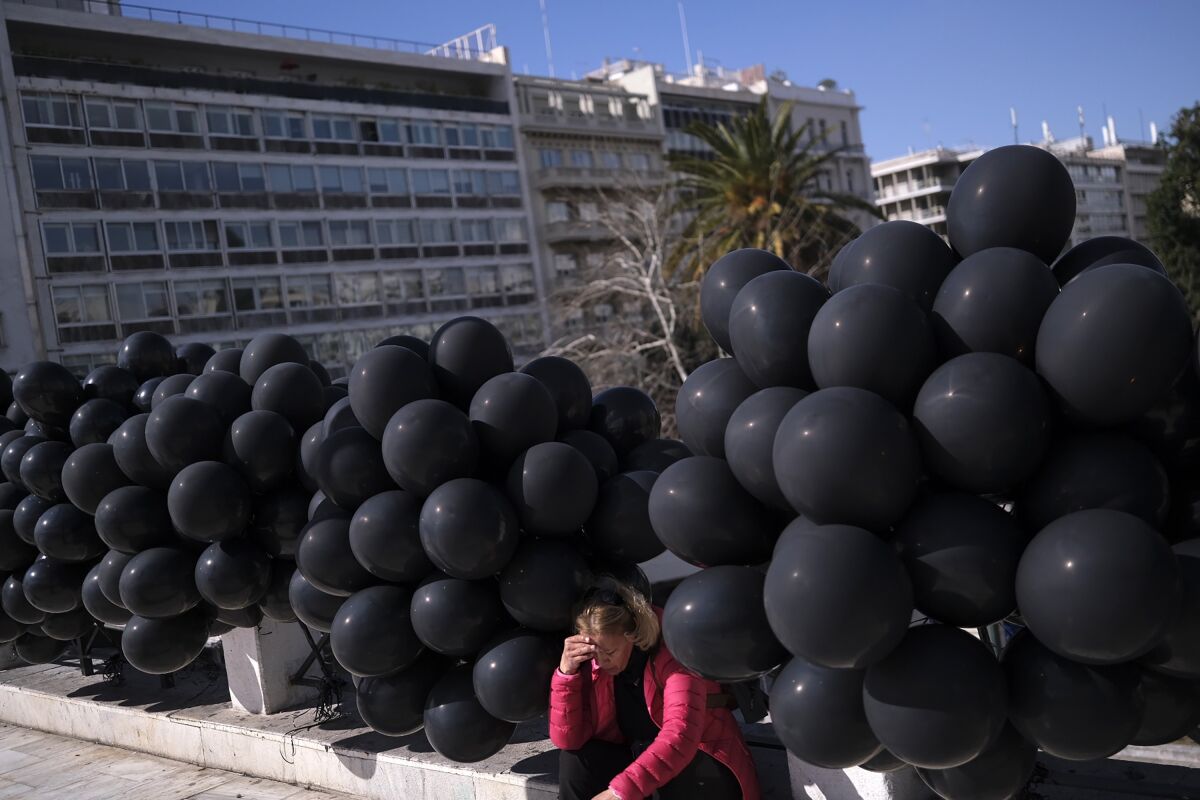 A woman sits among black balloons.