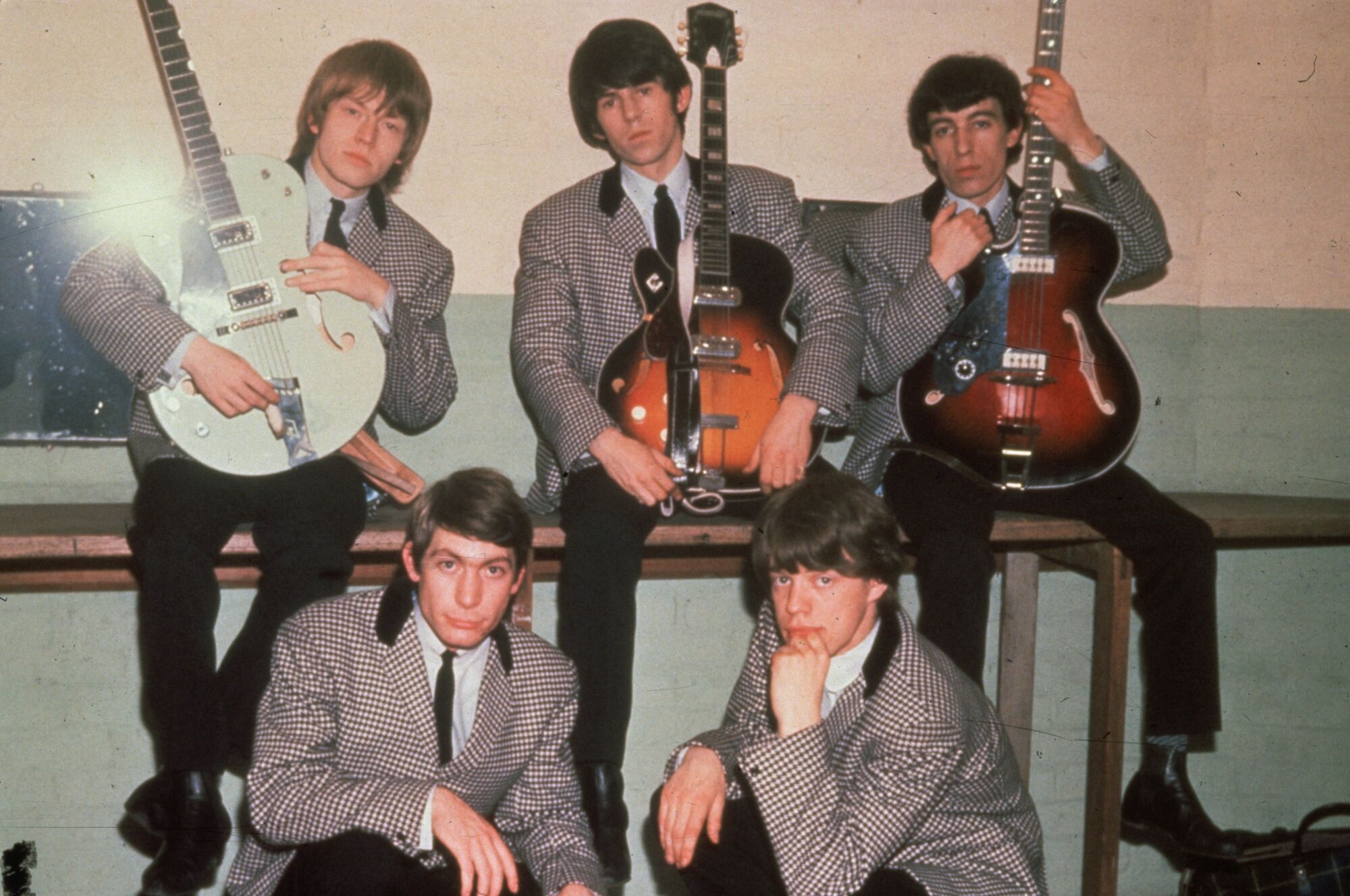 The Rolling Stones in 1964, wearing houndstooth suits, with three of them holding guitars.