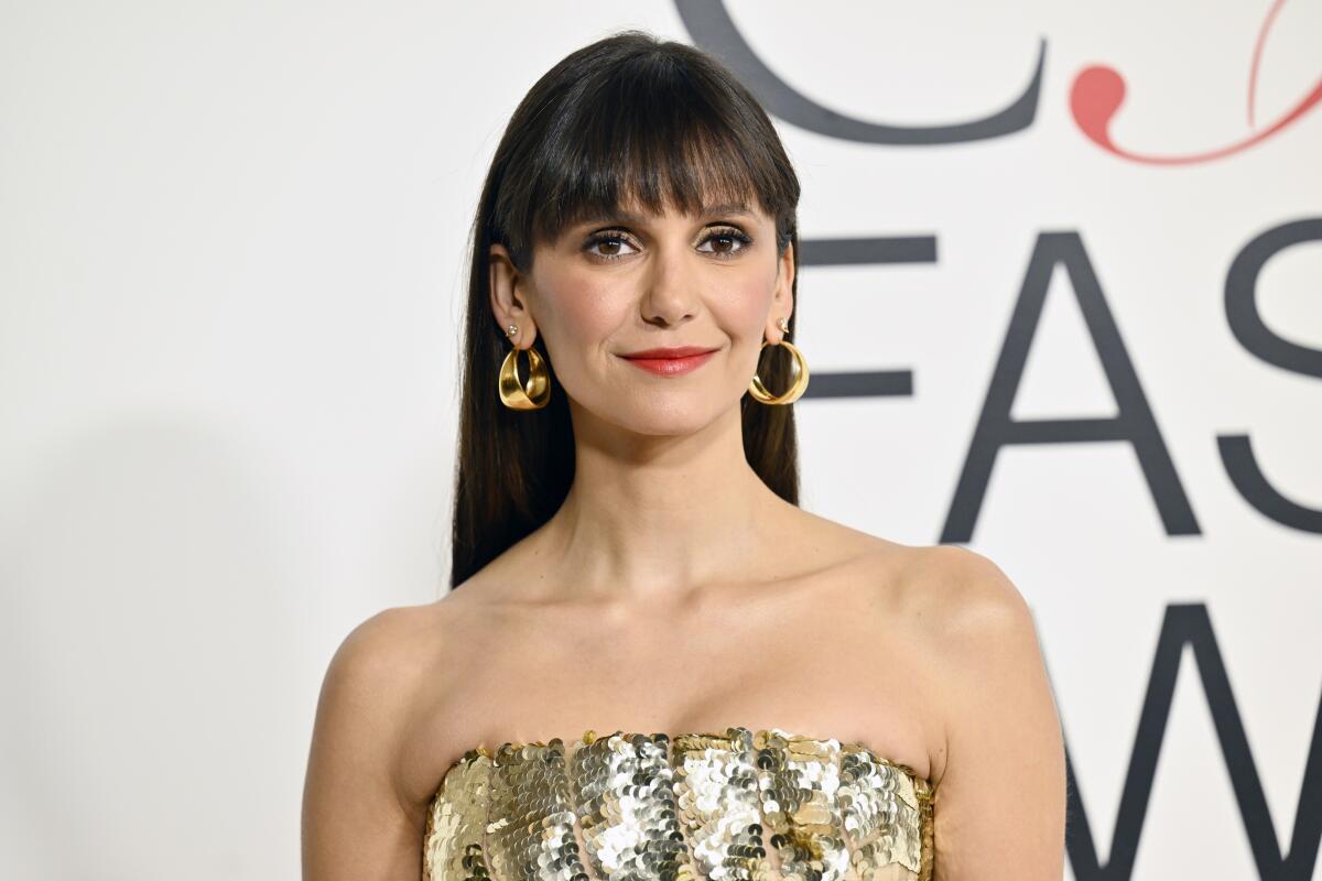 Nina Dobrev looking ahead with a calm smile on her face and long brown hair with bangs, clad in a sparkly strapless gown