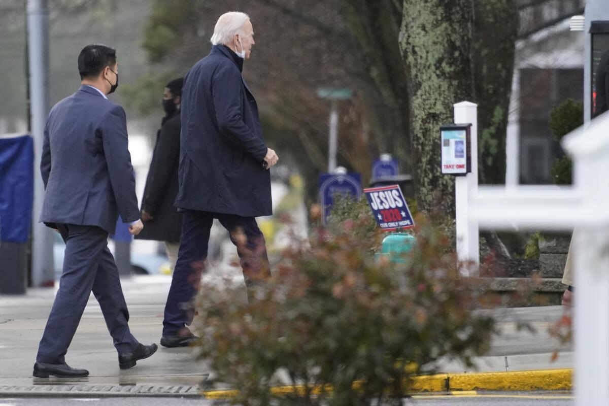 President-elect Joe Biden, followed by a Secret Service agent, walks along a sidewalk. A yard sign says "Jesus 2020."