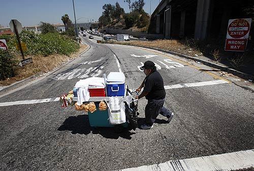 Street vendor Amado Campos, 44, of Los Angeles, who built his own rickety vending cart that tends to tip over and spill all his food and drinks, crosses a busy offramp near downtown Los Angeles.