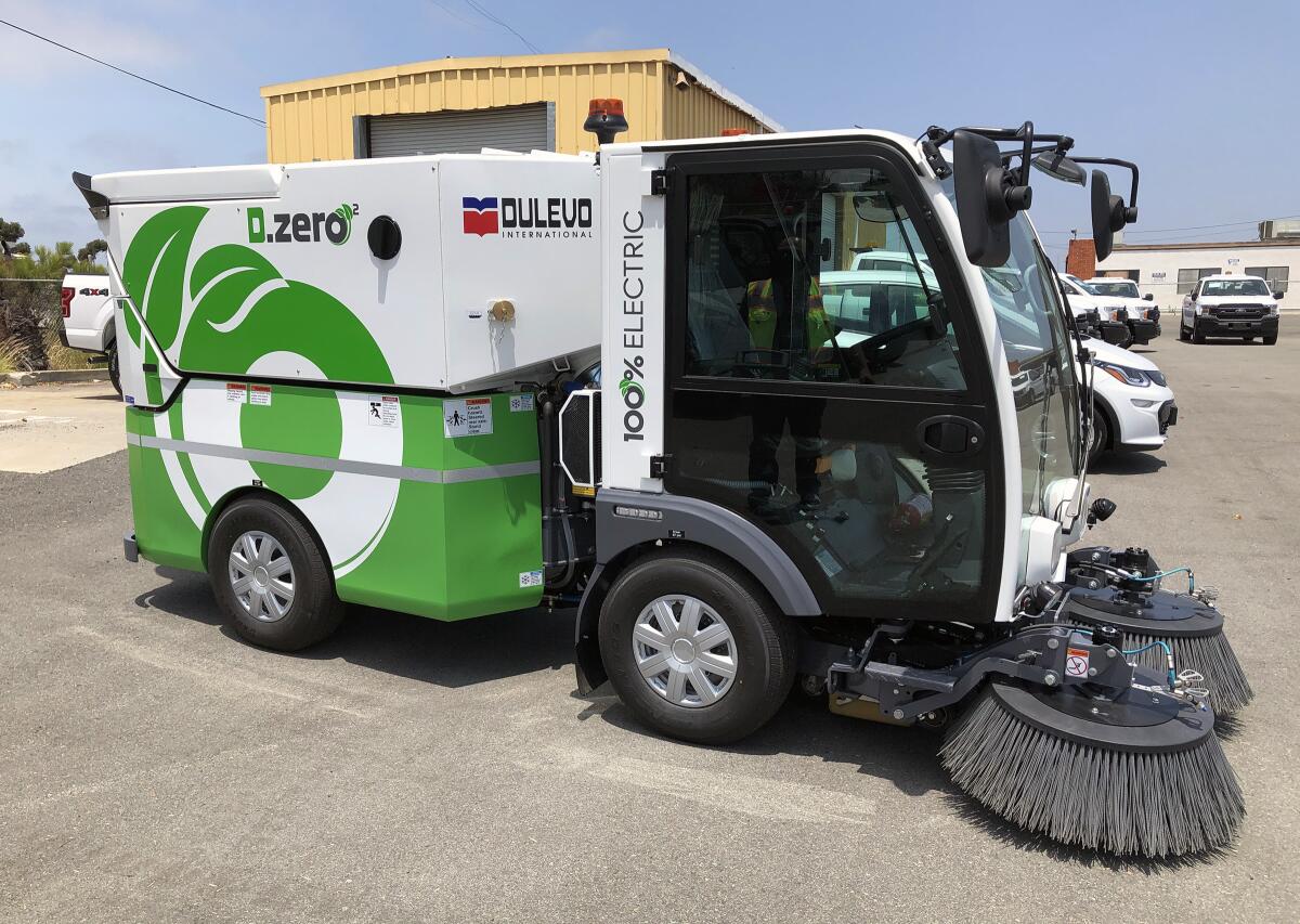 An electric mini street sweeper sits in a parking lot.