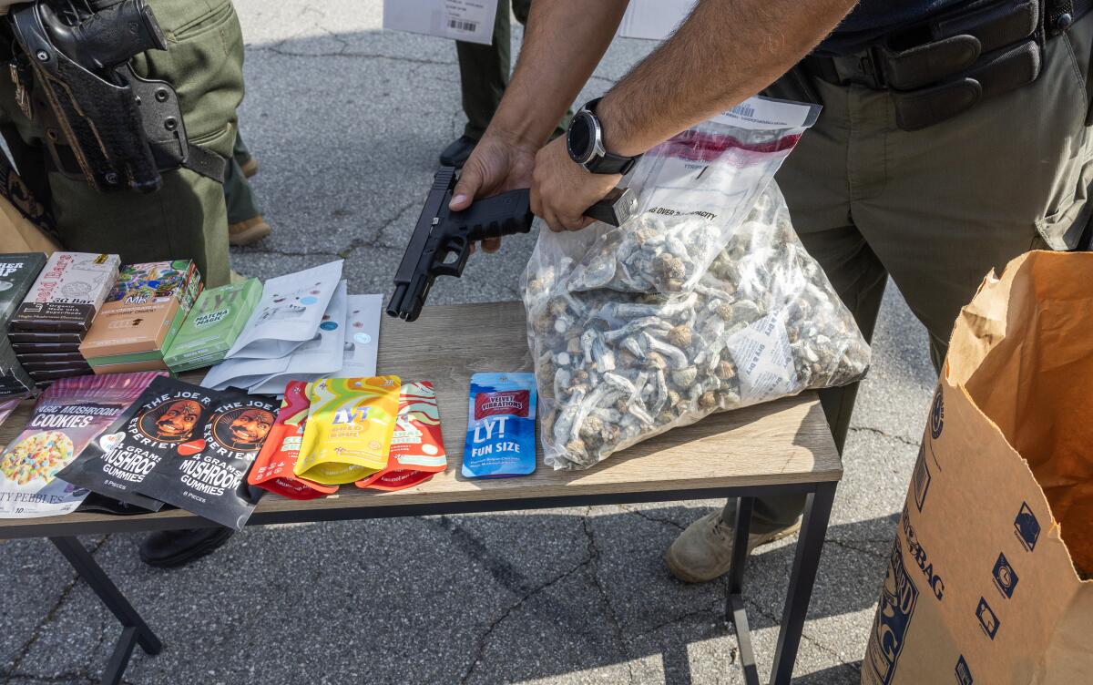 A person holds a gun over a table with packages and other things on it.