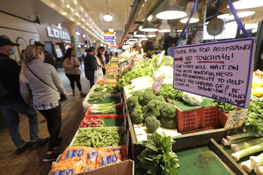 A sign at a produce stand reads "No Touching!" Tuesday, July 7, 2020, at Pike Place Market in Seattle. Tuesday was the first day of a new statewide order that requires people to wear masks or other facial coverings inside businesses in hopes of slowing the spread of the coronavirus. Business owners who fail to refuse service to customers who don't wear masks can face fines or lose their business license, but some business owners have raised concerns about turning away customers. (AP Photo/Ted S. Warren)