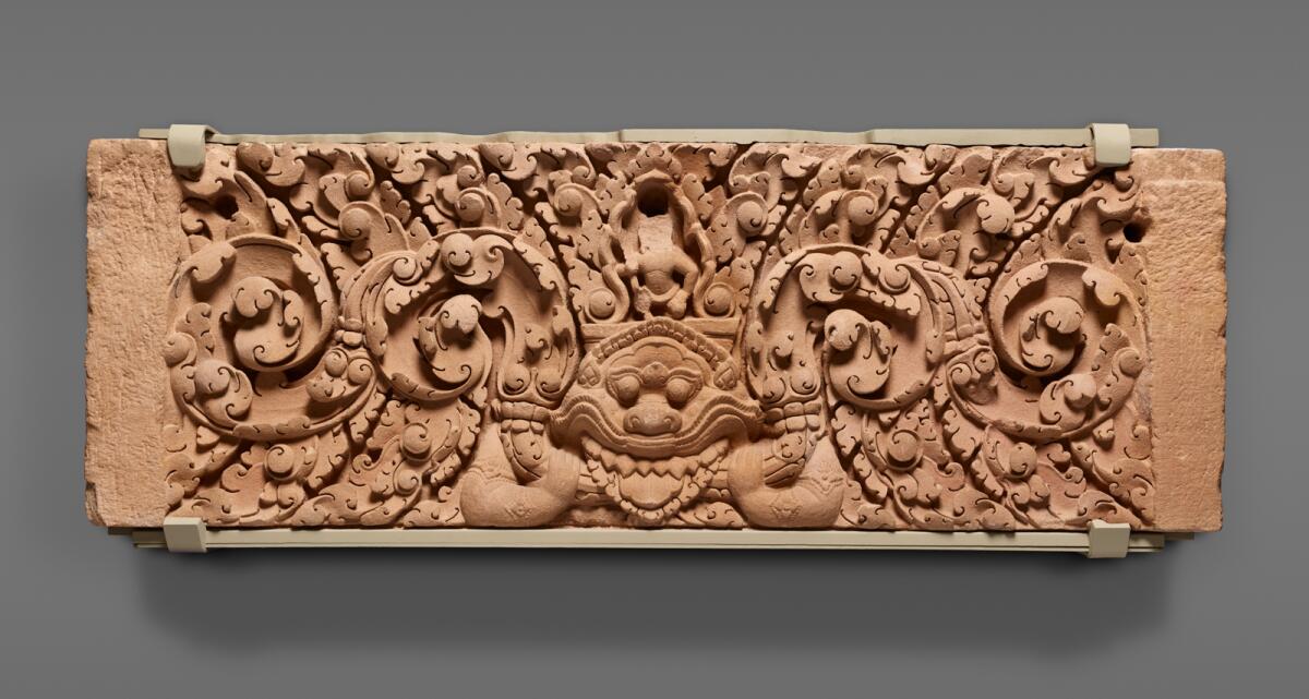 A stone carving shows a tiny faceless deity over a Kala image with garlands coming out of its mouth.