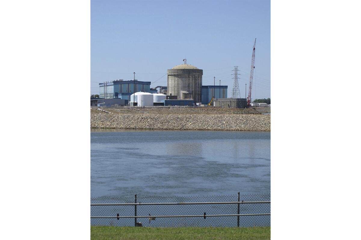 A brown cylindrical building sits amid shorter white ones and others near a body of water 