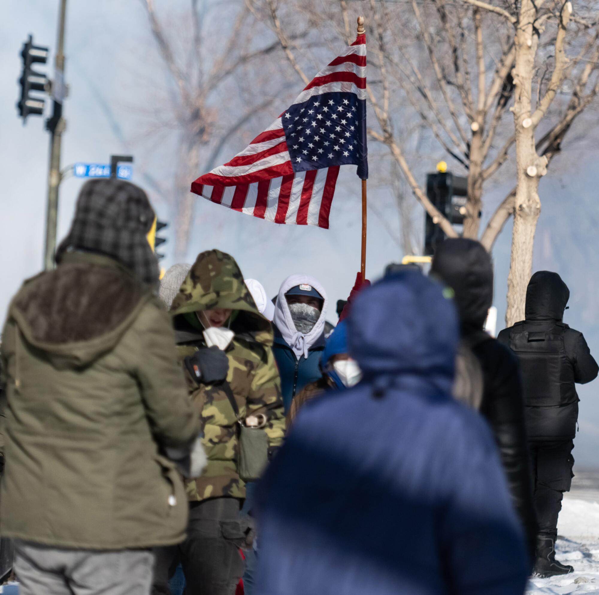 Protesters raise an inverted American flag as law enforcement officers launch tear gas canisters in Minneapolis.