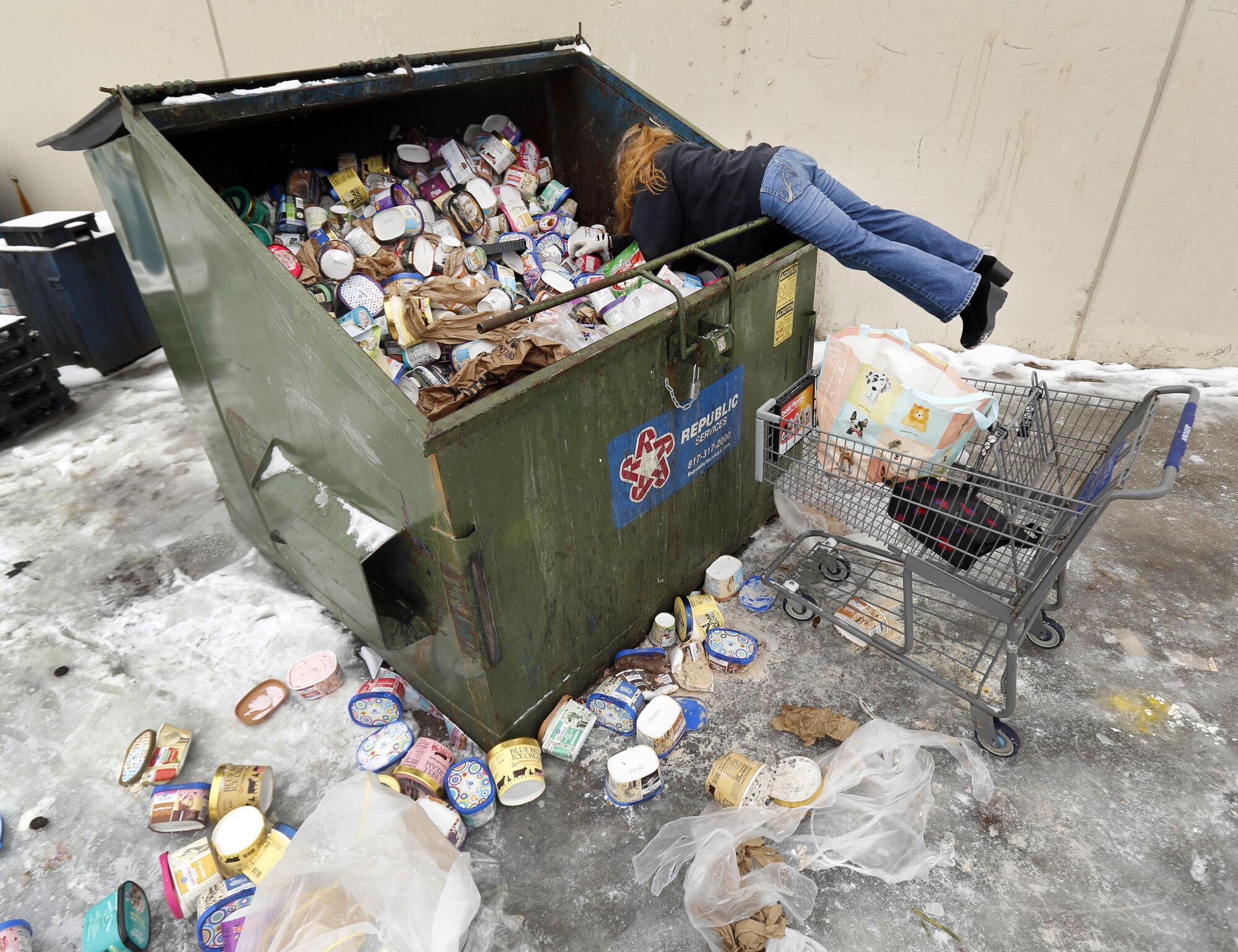A woman climbs into a dumpster.