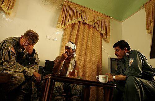 U.S. Army Capt. Dave Panian, left, bows his head in frustration as he negotiates with Col. Khalil, right, the district police chief of Farah city, through Panian's interpreter Zaki, center. Panian and his men had made a perilous journey to Farah to secure the monthly salaries for the Afghan police officers he is responsible for training.