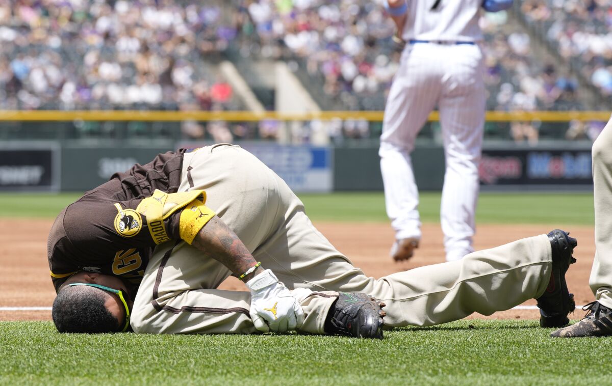 San Diego Padres' Manny Machado grabs his left ankle after being injured while trying to run out a ground ball hit to Colorado Rockies starting pitcher Antonio Senzatela in the first inning of a baseball game, Sunday, June 19, 2022, in Denver. Machado, who was called out on the play, was helped off the field. (AP Photo/David Zalubowski)