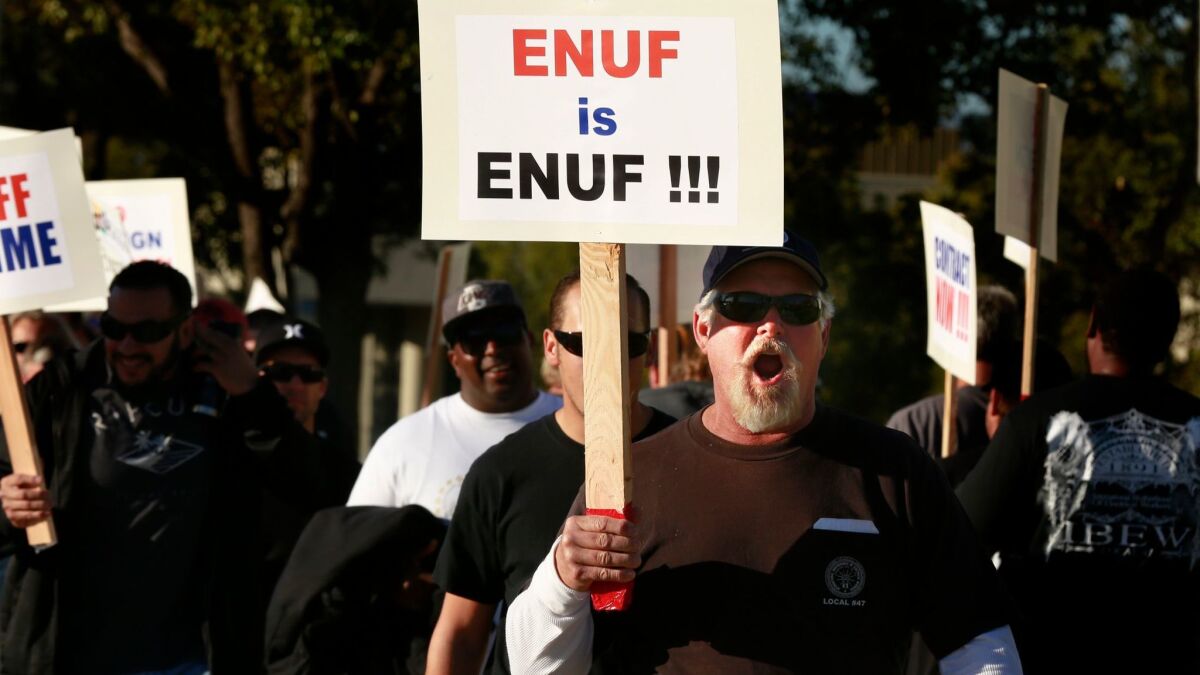 Members of the International Brotherhood of Electrical Workers walk the picket line in front of the Southern California Edison building in Irvine on Feb. 10, 2015, to protest plans by Edison to lay off workers in favor of replacements from India.