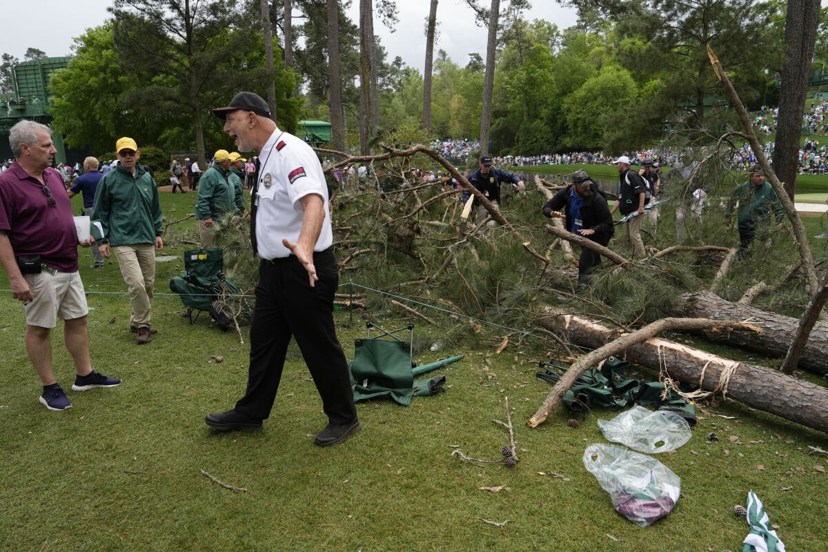 A security guard moves patrons away from trees that blew over on the 17th hole Friday.