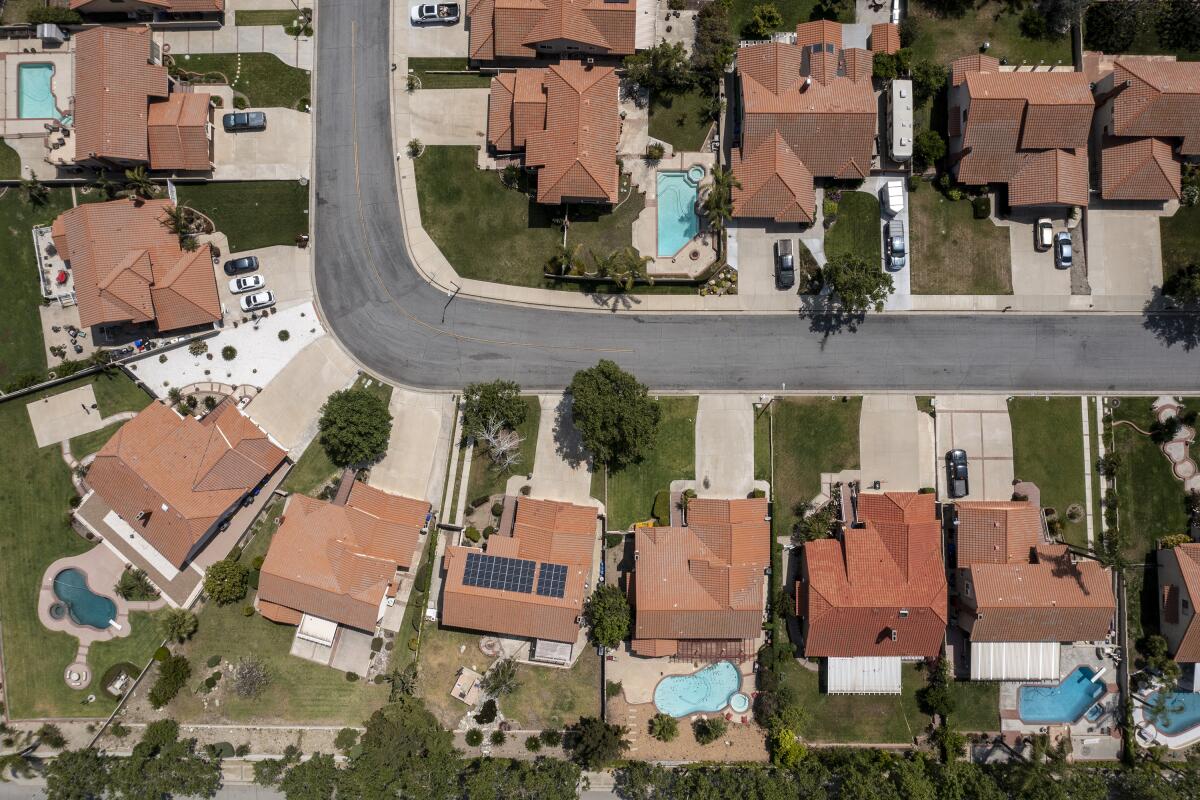 An aerial view of a single-homes neighborhood with lawns and pools. 