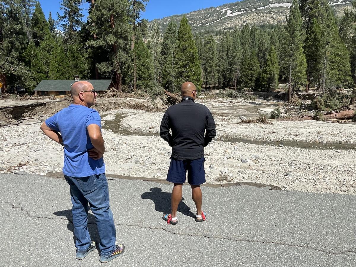 Two men stand and look at a washed-out parking lot at Camp River Glen.