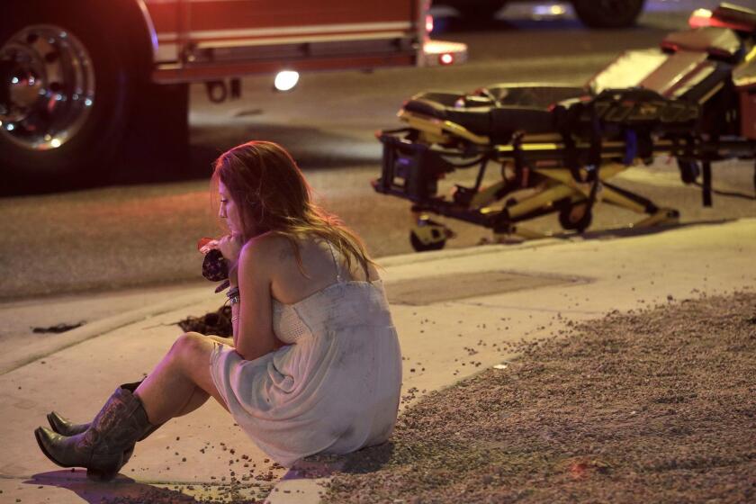 A woman sits on a curb at the scene of a shooting outside of a music festival along the Las Vegas Strip, Monday, Oct. 2, 2017, in Las Vegas. Multiple victims were being transported to hospitals after a shooting late Sunday at a music festival on the Las Vegas Strip. (AP Photo/John Locher)