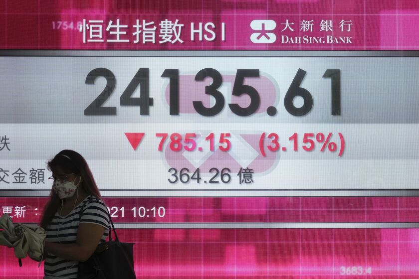 A woman walks past a bank's electronic board showing the Hong Kong share index at Hong Kong Stock Exchange in Hong Kong Monday, Sept. 20, 2021. Shares fell more than 3% in Hong Kong on Monday in holiday-thinned trading in Asia, with both Tokyo and Shanghai closed. (AP Photo/Vincent Yu)