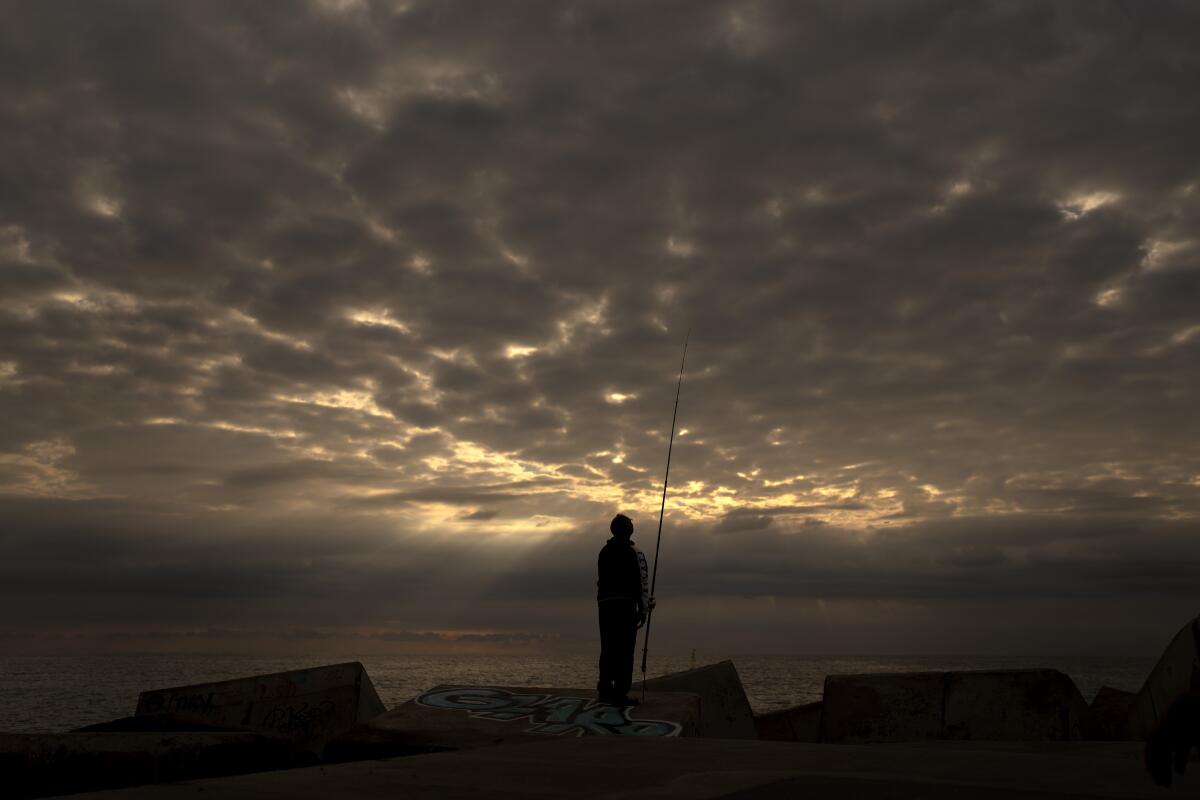 A man looks at his fishing rod on a breakwater in front of the mediterranean sea in Barcelona, Spain, Sunday, Oct. 10, 2021. (AP Photo/Emilio Morenatti)