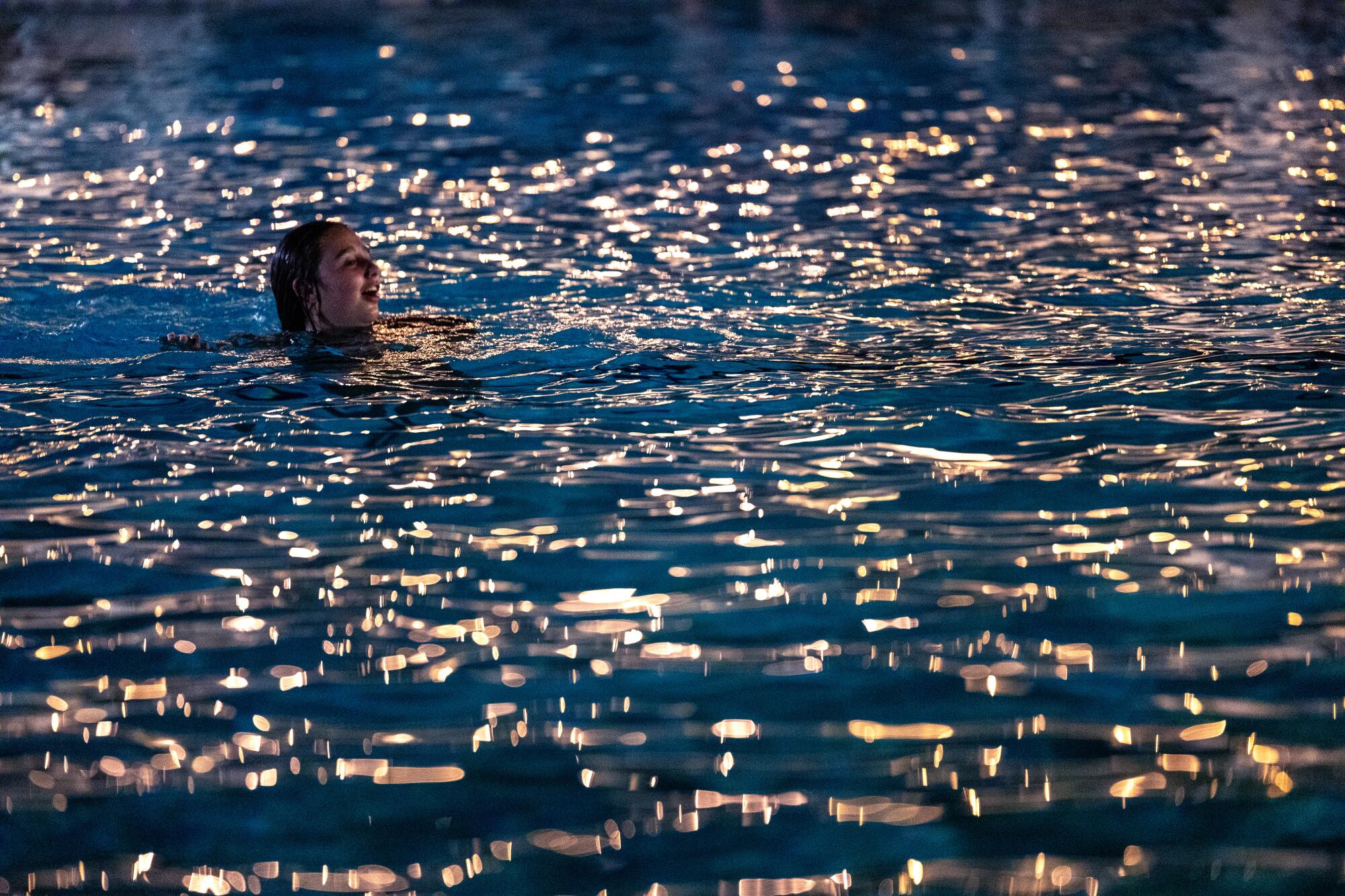 A man swims in a pool at night.