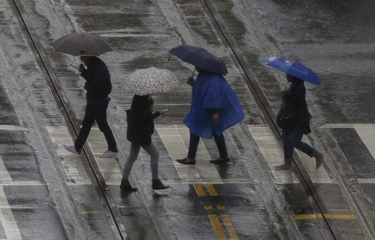 Pedestrians cross the street Friday in San Francisco. Storms brought rain and snow across California this weekend, and Southern California is dealing with another round of storms early Monday.