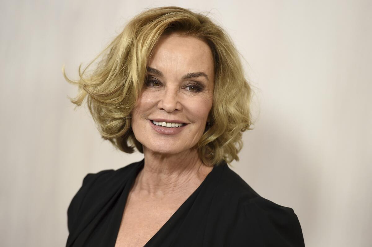 Jessica Lange wears her blond hair in a curled bob and smiles, looking off to the side. 