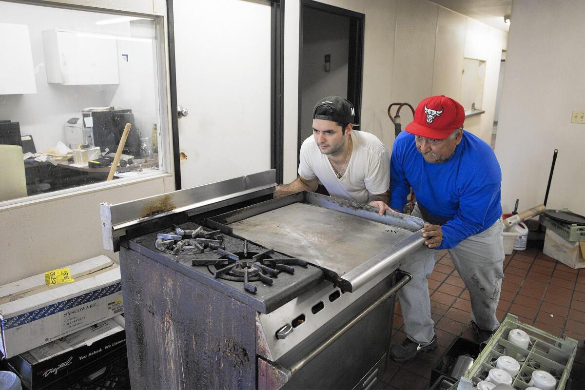 Antoine Challita, left, helps Jack Hernandez push a stove to his truck as the Challita family prepares to close Arnie's Manhattan Restaurant and Deli in Newport Beach on Friday.