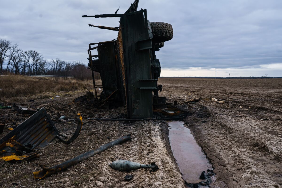  A burned and overturned truck lies on its side in the field with explosive munition spilled out and scattered around it