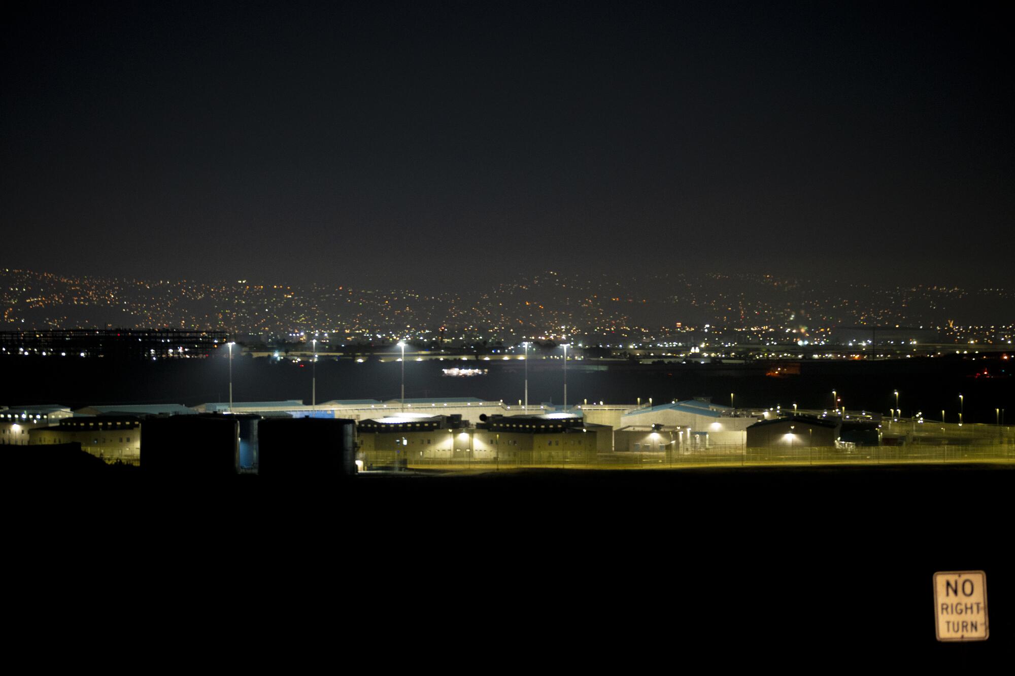 Otay Mesa Detention Center at night with the lights of Tijuana visible in the distance behind the building
