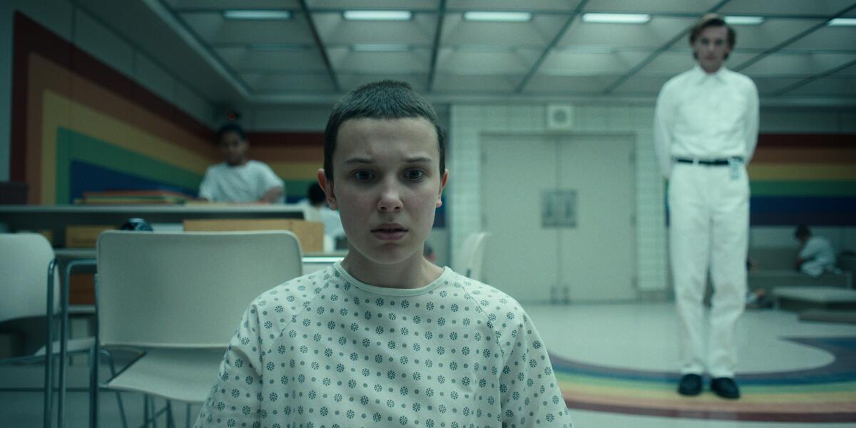A young girl wears a hospital gown in an institutional setting in a scene from "Stranger Things."