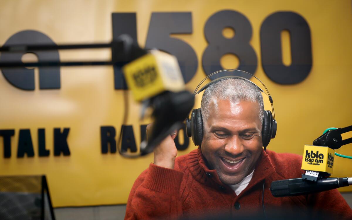 A man wearing headphones smiles in front of a microphone.