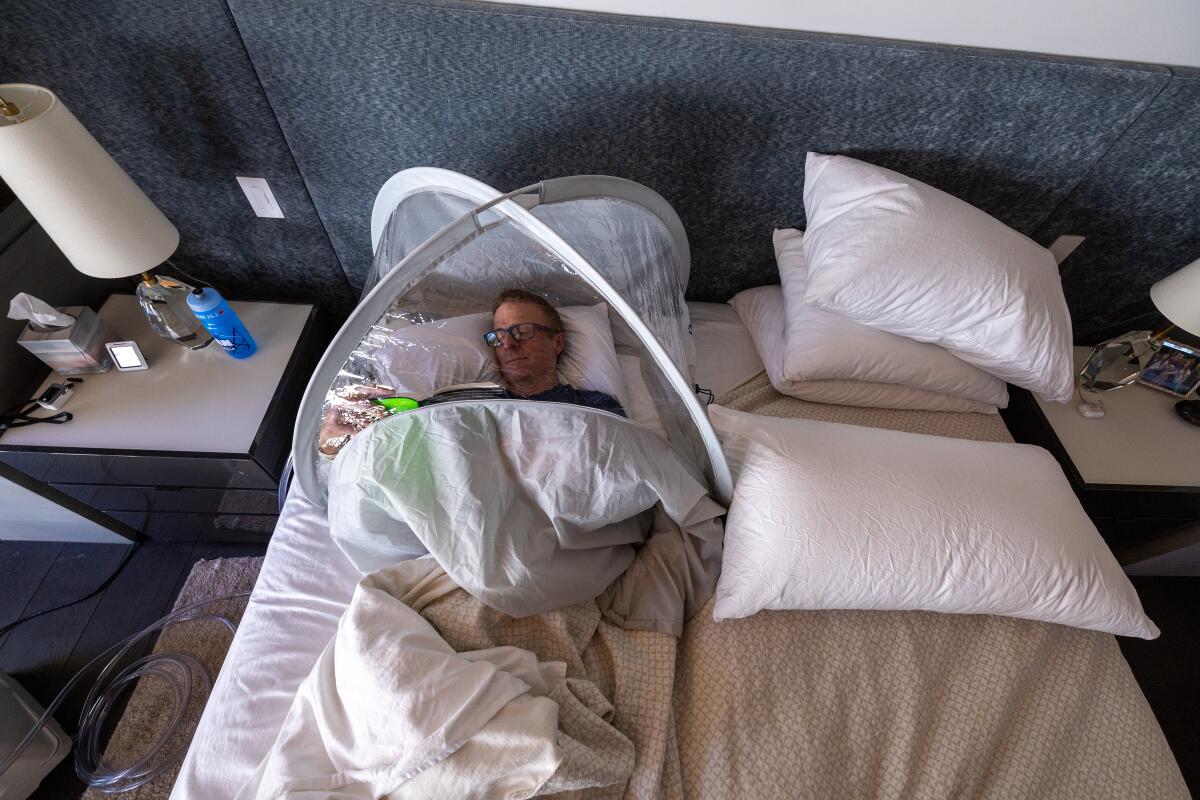 一名男子躺在床上看书，头被盖在塑料帐篷里。