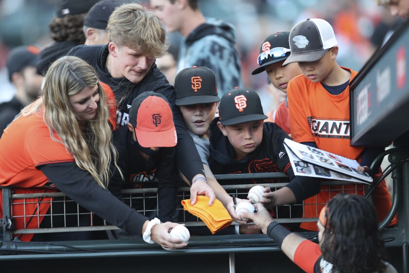FILE - San Francisco Giants' Brandon Crawford, bottom, signs autographs for fans before Game 2 of a baseball National League Division Series against the Los Angeles Dodgers on Oct. 9, 2021, in San Francisco. Even if baseball’s first work stoppage in 26 years doesn’t result in missed games, the league and its players are at risk of alienating their next wave of fans. (AP Photo/Jed Jacobsohn, File)