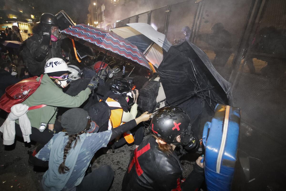 Demonstrators shield themselves with umbrellas as federal officers launch tear gas in Portland, Ore.