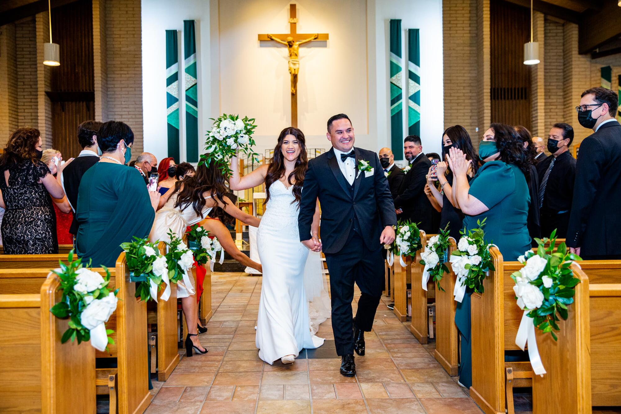 A bride and groom walk down the aisle of a church as people in the pews applaud them.