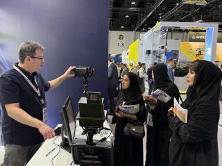 Women in dark robes and headscarves look at equipment displayed by a man behind a counter
