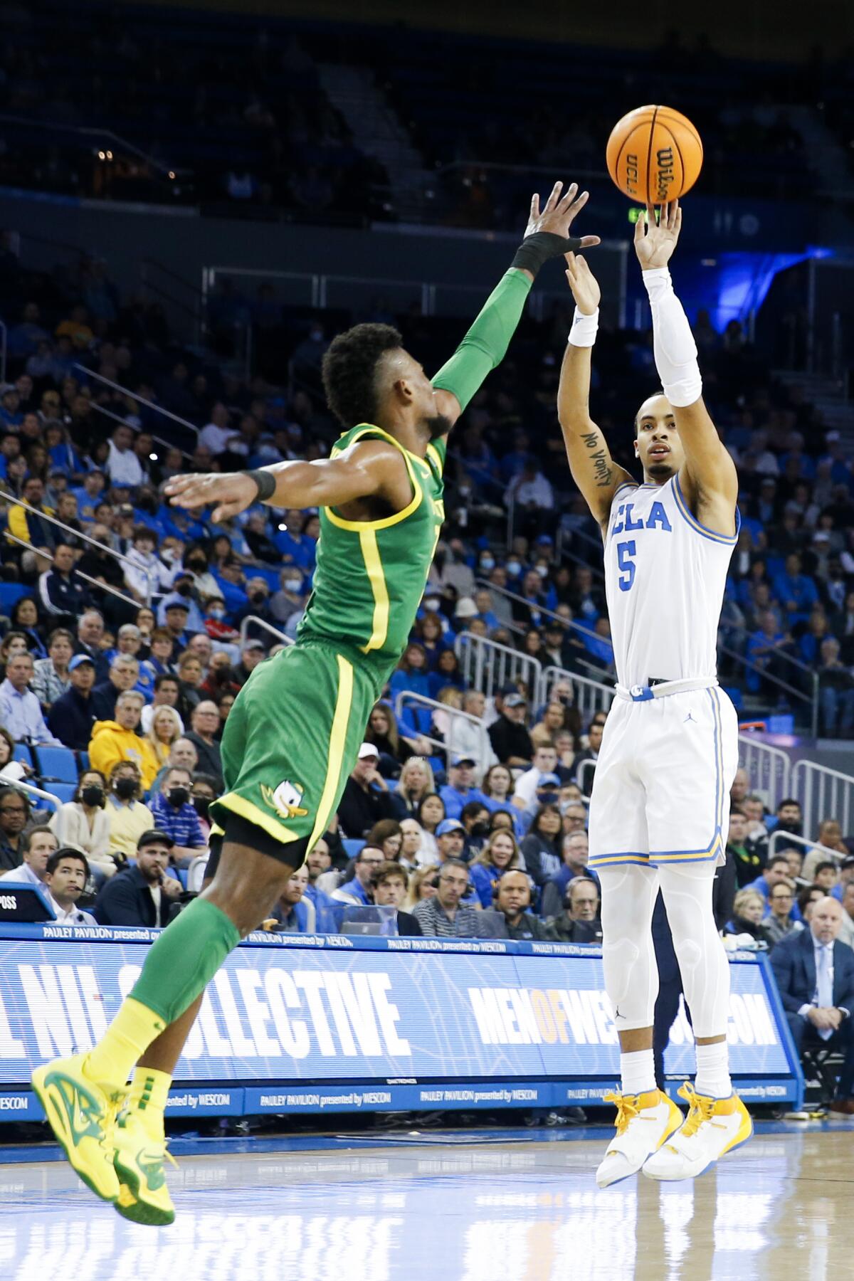 Bruins guard Amari Bailey releases a three-point shot while defended by Ducks forward Quincy Guerrier.
