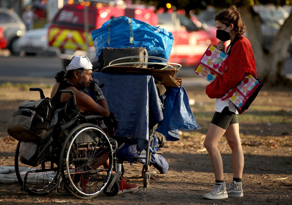 An outreach worker talks with a homeless man sitting in a wheelchair.