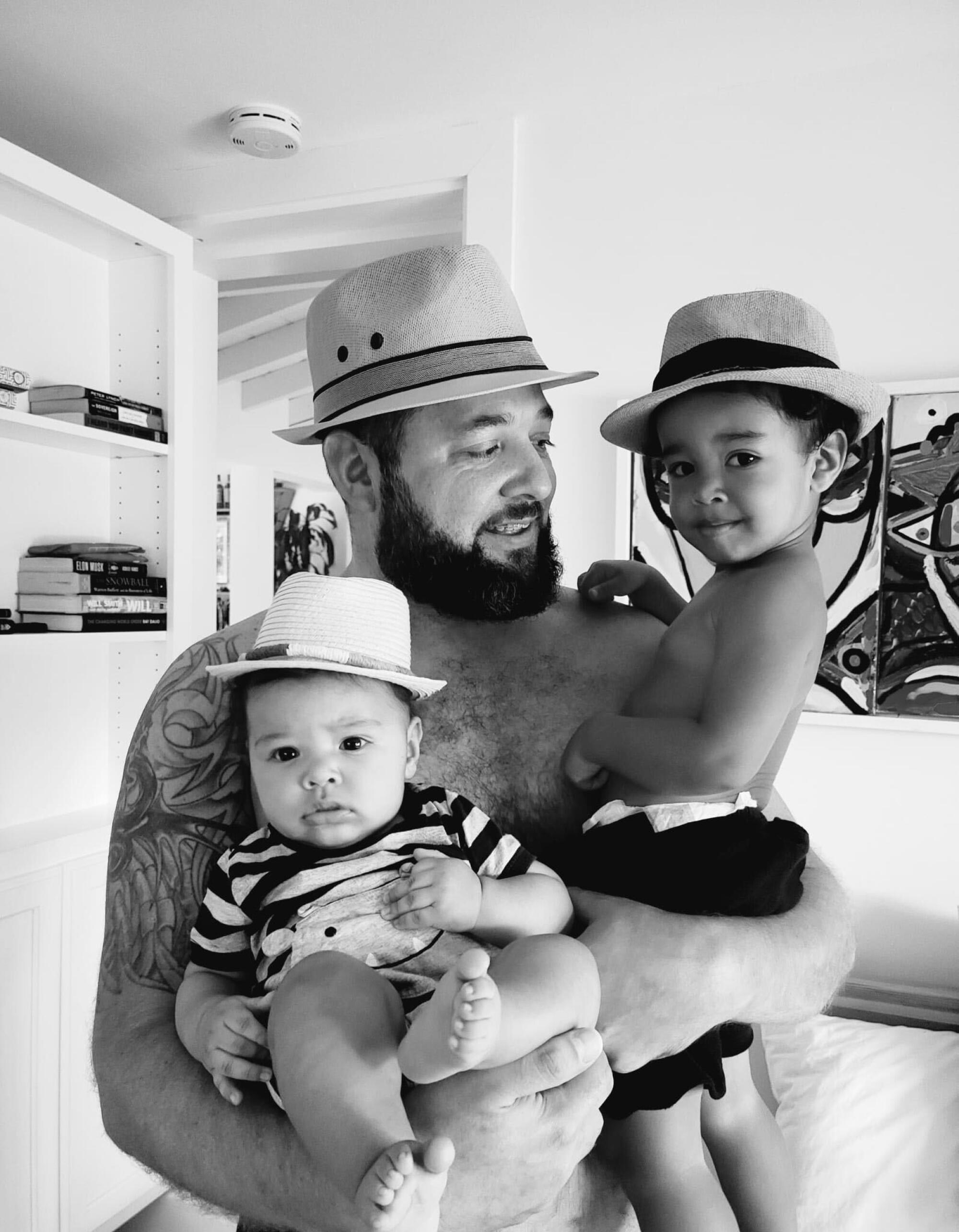 Jesse Saenz holds his sons Enso, right, and Airo. They are wearing hats.