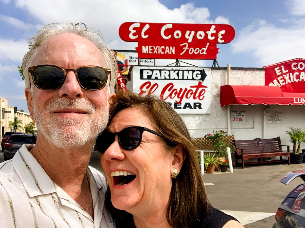 A smiling man and woman, both wearing sunglasses, outside El Coyote.