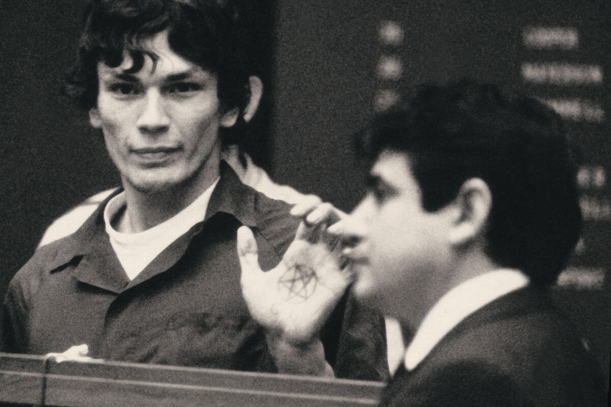 A man with a pentagram on his hand holds it up in a courtroom.