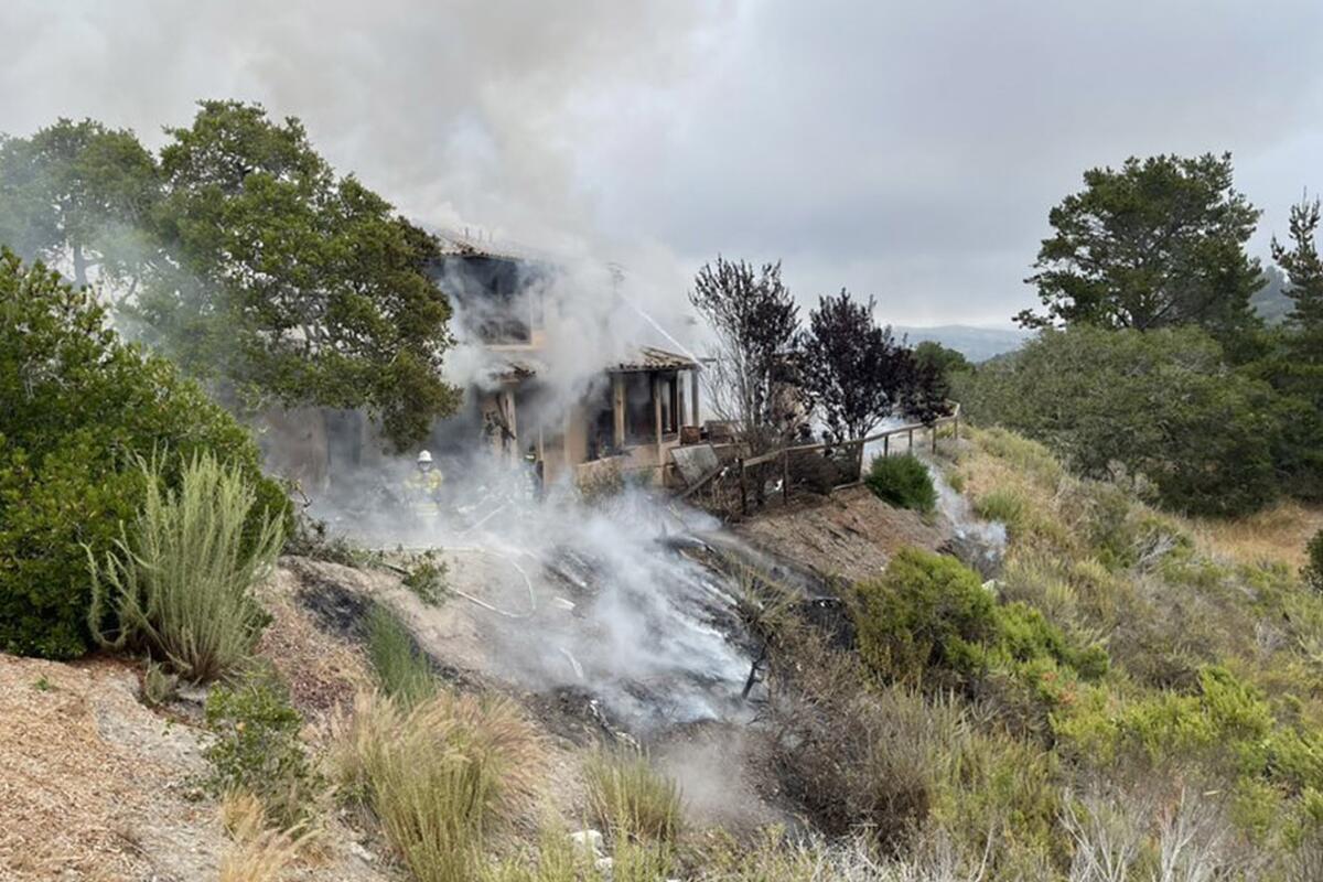 A house smolders amid smoke on a hillside.