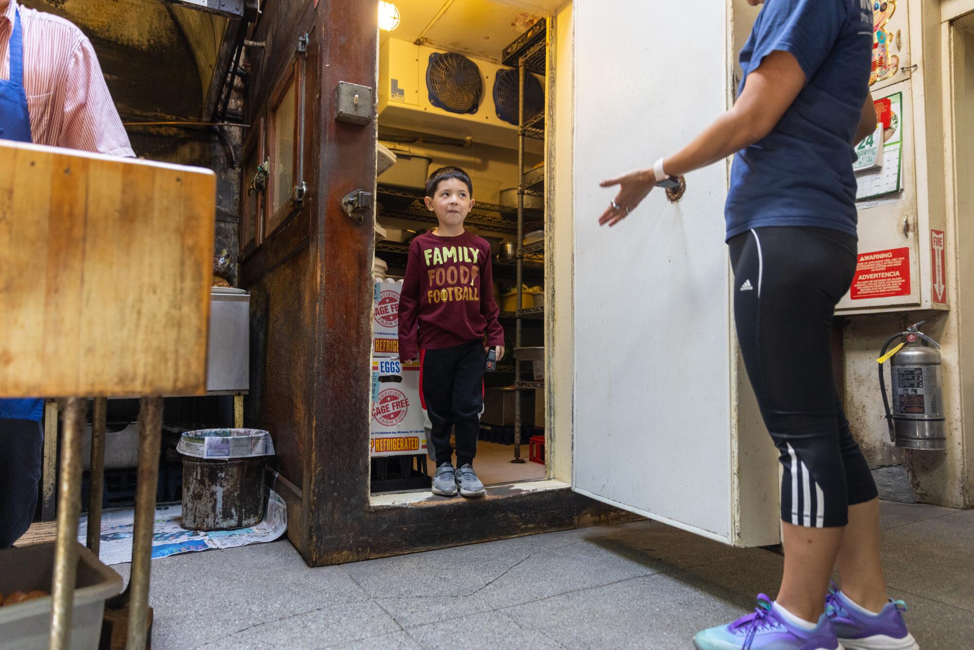 A young boy stands inside the cooler in a restaurant kitchen. 