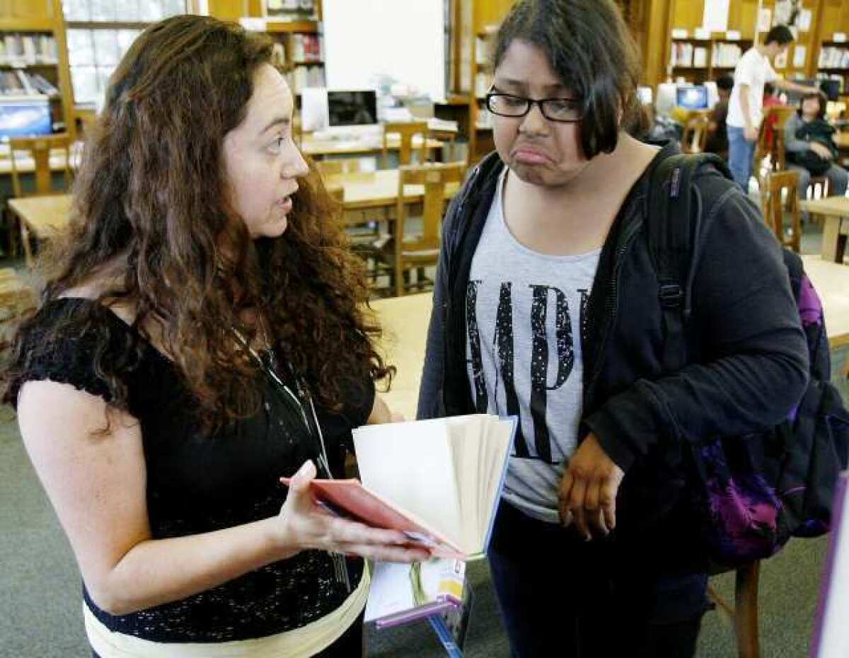 Librarian Maura Large shows Emely Arroyo, 13, the book "Hoot" by Carl Hiaasen in the library in Eliot Middle School in Altadena. Large has been a librarian at the school for two years and could be laid off this year. District officials have proposed to eliminate seven teacher-librarian positions, and the Glendale school district has proposed to eliminate four.