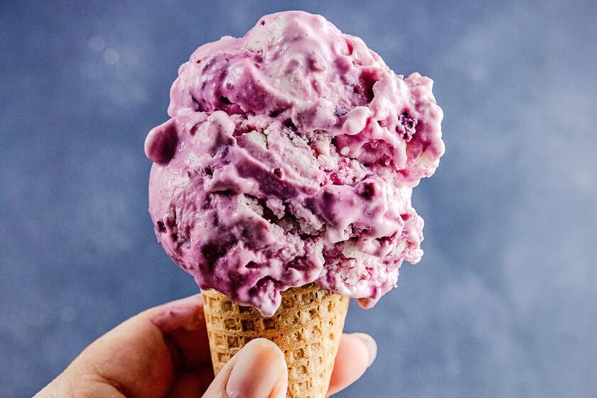 A hand holding a cone of cherry vanilla frozen yogurt.