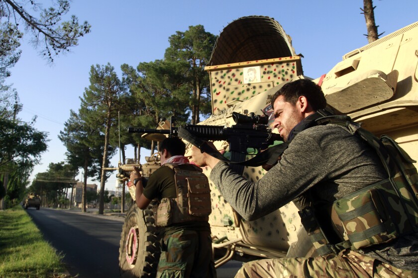 Two men in camouflage clothing aim their weapons next to a military vehicle