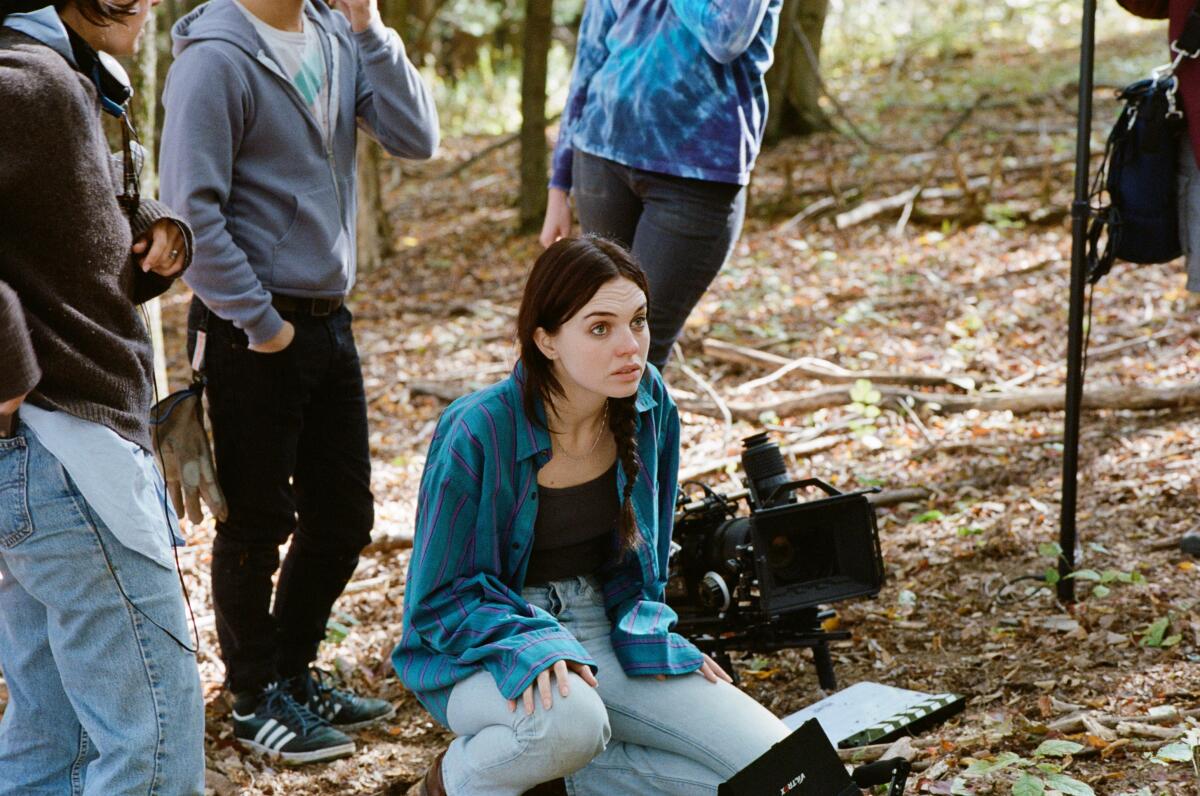 A woman sits on the ground outside, on a film set.