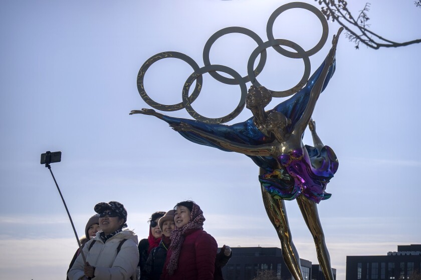 Visitors pose for a selfie with a statue containing the Olympic rings at a park near the headquarters for the Beijing Organizing Committee for the Olympic Games (BOCOG) in Beijing, Thursday, Dec. 16, 2021. Beijing Winter Olympics organizers say measures to prevent cross-infections between athletes and the outside world are being extended to holding their garbage inside the bubble dividing the two. (AP Photo/Mark Schiefelbein)